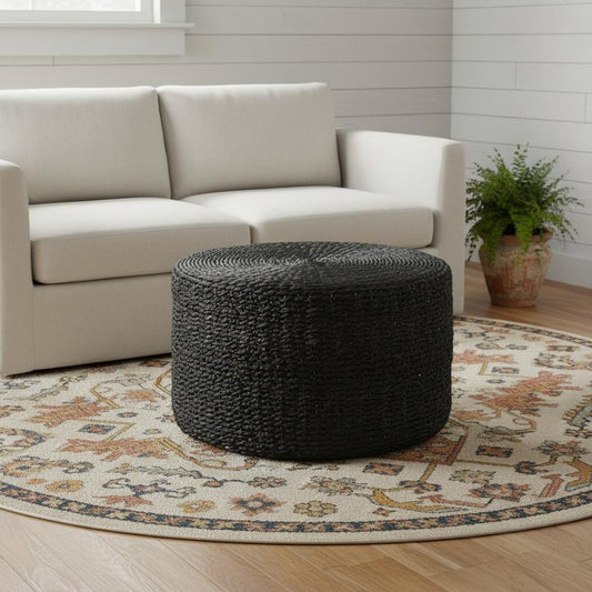 Black woven ottoman in a living room with a beige sofa and decorative rug.