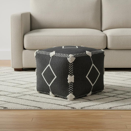 Black patterned ottoman in front of a beige sofa on a wooden floor.