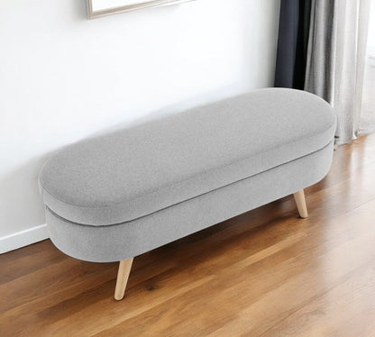 Gray upholstered bench with wooden legs on a wooden floor.