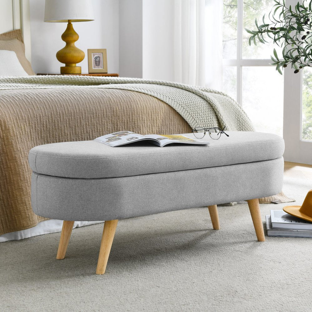 Gray upholstered bench with wooden legs in a bedroom setting.